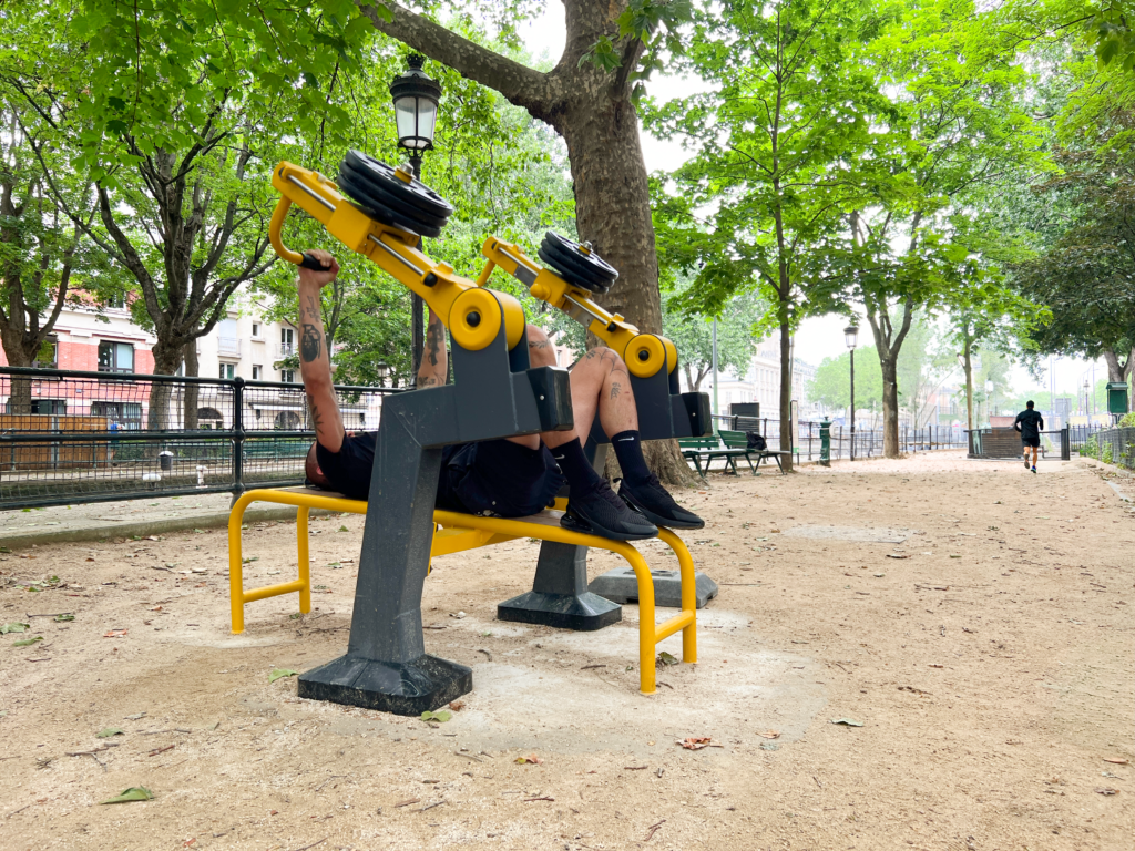 Adulte pratiquant le fitness en plein air sur des équipements extérieurs. Dynamisation de la vie étudiante par le sport en extérieur.