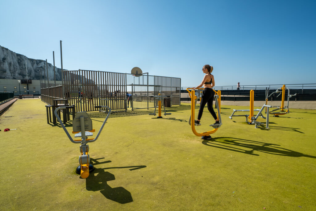 Femme pratiquant le fitness en plein air sur des équipements extérieurs. Dynamisation de la vie étudiante par le sport en extérieur.