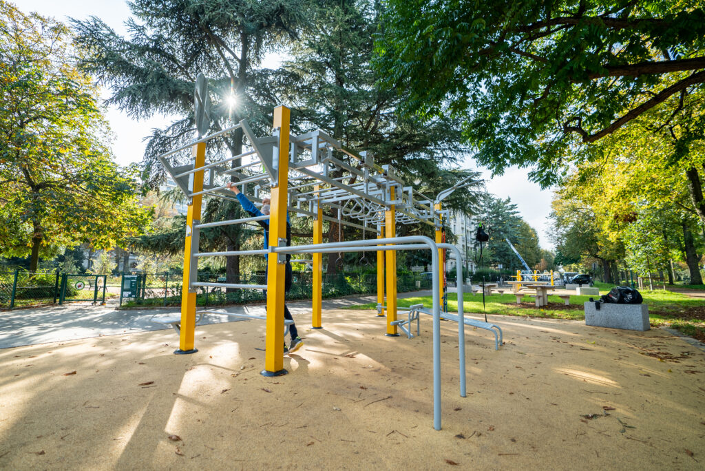 Adulte pratiquant le fitness en plein air sur des équipements extérieurs. Dynamisation de la vie étudiante par le sport en extérieur.