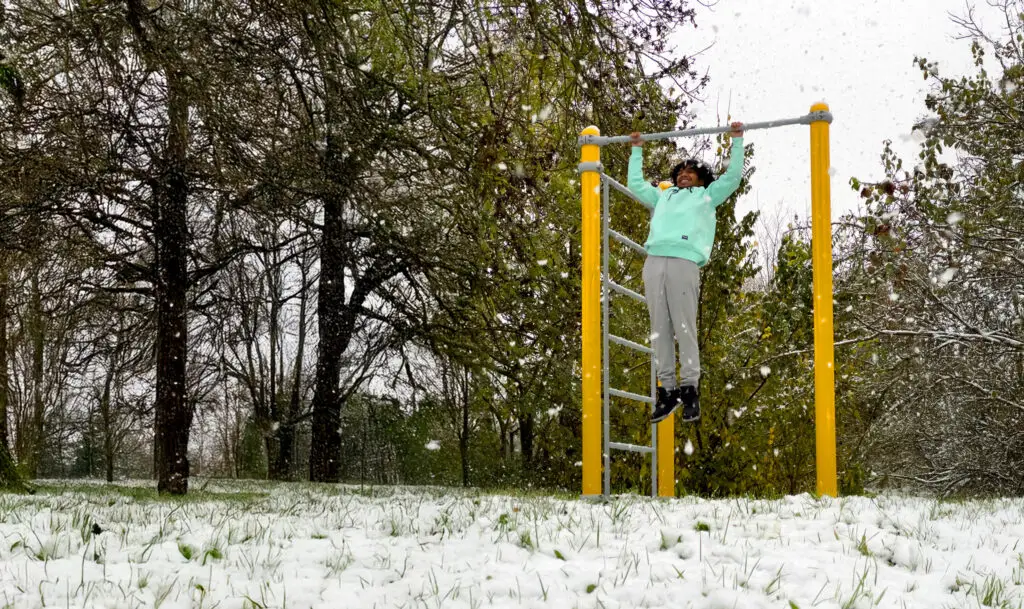 Étudiant pratiquant le fitness en plein air dans la neige sur des équipements extérieurs. Dynamisation de la vie étudiante par le sport en extérieur.