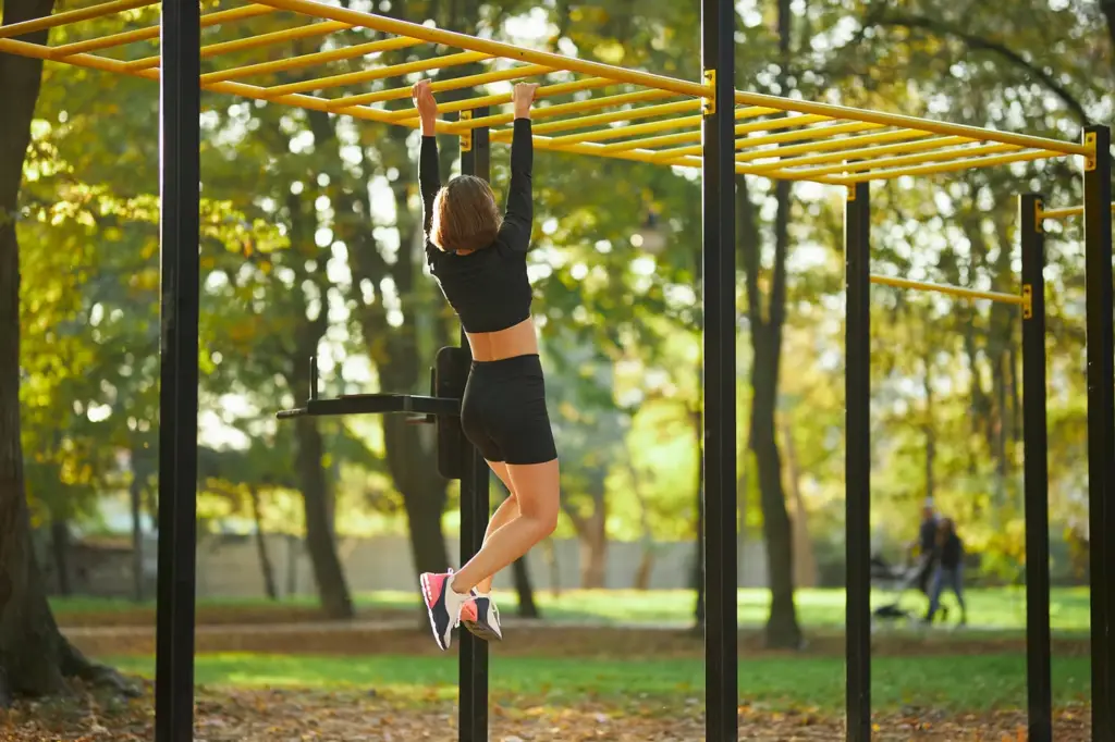 Femme pratiquant le street workout sur des barres parallèles en extérieur. Illustration de l'essor du street workout féminin.